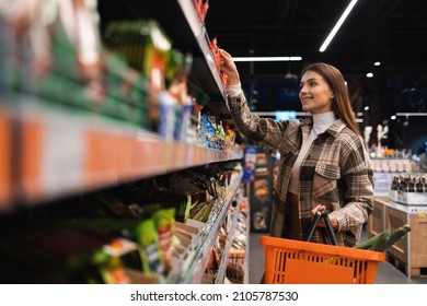 Happy young woman looking at product at grocery shop. Customer buying food at the supermarket - Shutterstock ID 2105787530