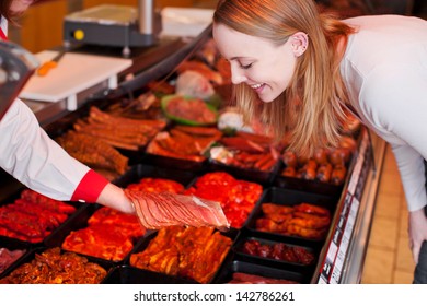 Happy young woman looking at sliced meat on butcher hand at supermarket - Powered by Shutterstock