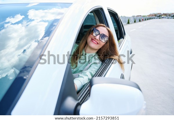 Happy young woman looks out the window of a new\
car or a rental car. The concept of buying a new car, renting and\
freedom of movement