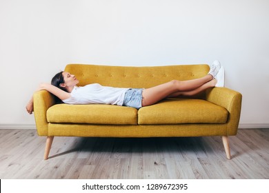 Happy young woman lying on couch and relaxing at home