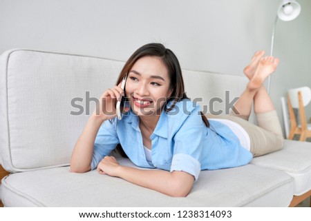 Happy young woman lying on the couch at home, talking on the phone with friend
