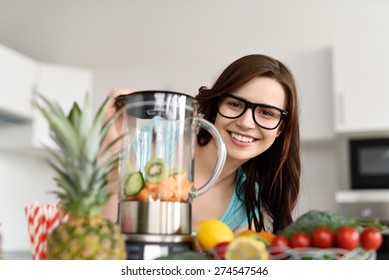 Happy young woman making healthy fruit smoothies in her kitchen peeking around the liquidizer and fresh fruit ingredients with a friendly smile - Powered by Shutterstock