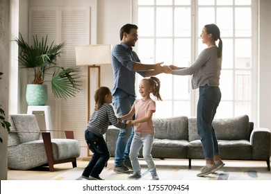 Happy Young Woman With Man And Adorable Little Daughter And Son Holding Hands, Dancing To Favorite Music, Having Fun In Living Room, Laughing Mother And Father Celebrating Event With Children