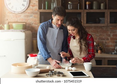 Happy Young Woman And Man Baking Pie In Loft Kitchen. Young Family Cooking At Home, Using Digital Tablet. Mockup For Recipe