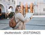 Happy young woman with map in old town. Holidays and tourism concept. Female tourist searching direction on location map while traveling abroad in autumn.