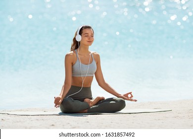 Happy young woman meditating at the seacoast. Girl practicing yoga on the beach at sunrise. Shallow DOF copy space sea background. Music for meditation creative concept