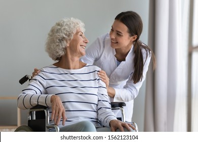 Happy Young Woman Nurse Help Disabled Paralyzed Senior Grandma Patient Sit On Wheelchair At Home Hospital, Female Carer Provide Old Lady Medical Service, Elder People Healthcare Concept