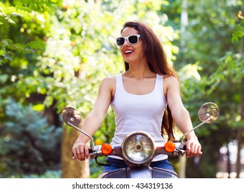 The Happy Young Woman On The Scooter In City Park In The Summer Time