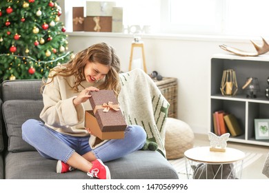 Happy Young Woman Opening Christmas Gift At Home