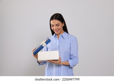 Happy young woman opening gift box on light grey background - Shutterstock ID 2250497799