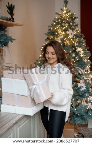 Happy young woman opening gifts and presents near Christmas tree at home. Holidays and traditions concept 