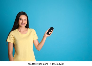 Happy young woman operating air conditioner with remote control on light blue background. Space for text