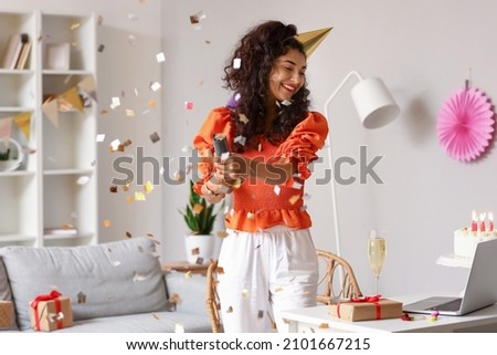 Happy young woman with party popper celebrating birthday at home