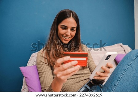Happy young woman paying a purchase with credit card at home. Female smiling holding a creditcard and doing a payment transaction on ecommerce app with a cell phone. Banking online concept. High