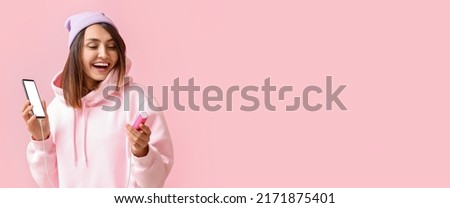 Happy young woman with phone and power bank on pink background with space for text