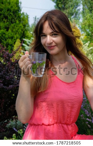 A happy young woman in a pink dress on a sunny morning in the Ukrainian garden. Woman holding a glass of herbal drink. Close up. Vertical image.