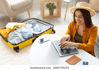 Happy young woman planning vacation travel with laptop pc, reading tourist blog online, booking tickets or hotel room on web, getting ready for abroad journey at home, free space