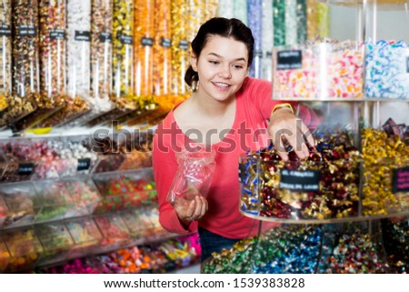 Happy young woman posing to photographer picking different candies with  scoop in  cellophane bag