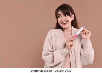 Happy young woman with pregnancy test on light brown background, space for text - Powered by Shutterstock