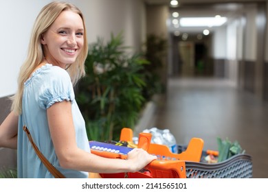 Happy Young Woman Pushing Trolley In Supermarket