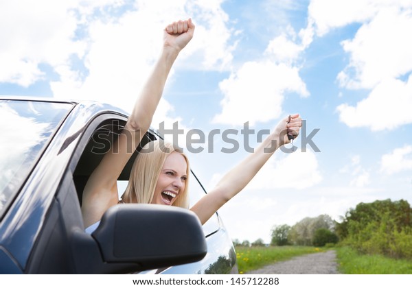 Happy Young\
Woman Raising Hand Out Of Car\
Window