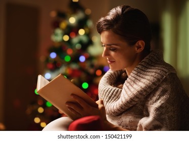 Happy Young Woman Reading Book In Front Of Christmas Tree