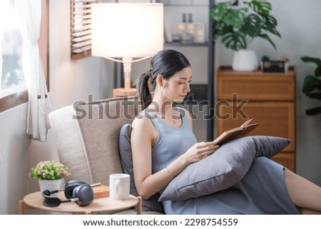 Happy young woman reading book on sofa at home. Lifestyle freelance relax and chill drinking coffee in living room. Lifestyle Concept