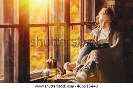 Happy young woman reading a book by the window in the fall