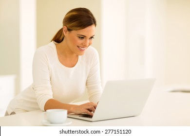 glückliche junge Frau, die auf dem Laptop-Computer in der Küche E-Mails liest