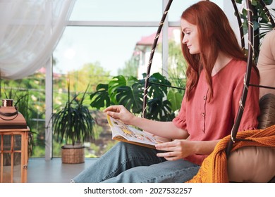 Happy Young Woman Reading Magazine In Egg Chair At Indoor Terrace