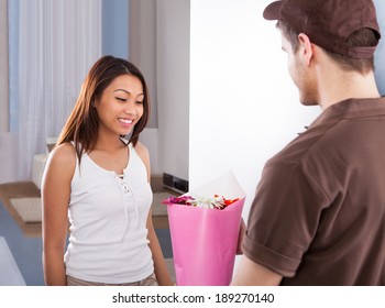 Happy Young Woman Receiving Flower Bouquet From Delivery Man At Home