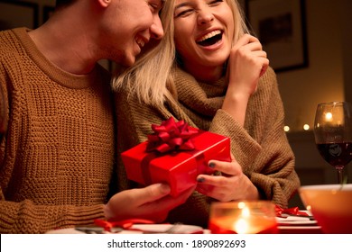 Happy young woman receiving gift box from loving man. Couple in love having fun celebrating Valentines day enjoying romantic dinner date holding present sit at home table. Surprise on Valentine's Day. - Powered by Shutterstock