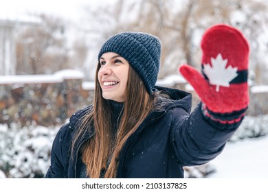 Happy young woman in red mittens with the flag of Canada in snowy weather.
