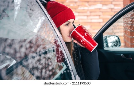 Happy Young Woman With A Red Thermo Cup Sits In A Car In Winter.