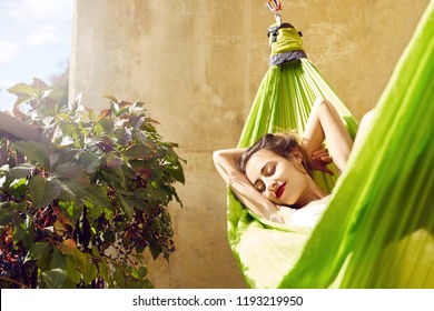 happy young woman relaxed lies in a hammock on the balcony House. Woman basks and sunbathes in a hammock - Powered by Shutterstock