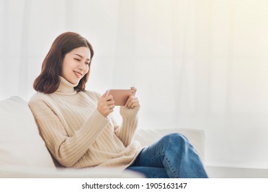 Happy Young Woman Relaxing On  Couch And Watching The Mobile Phone