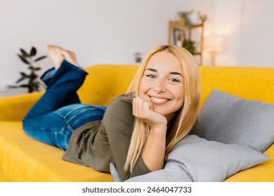 Happy young woman relaxing on her couch at home in the living room. Smiling portrait of blonde female looking at camera lying on sofa. - Powered by Shutterstock