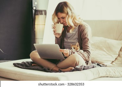 Happy young woman is relaxing on comfortable couch and using laptop at home. Photo toned.