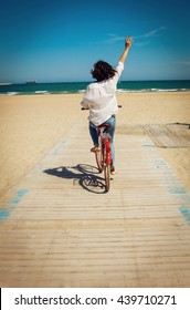 Happy Young Woman Riding A Bike On A Beach