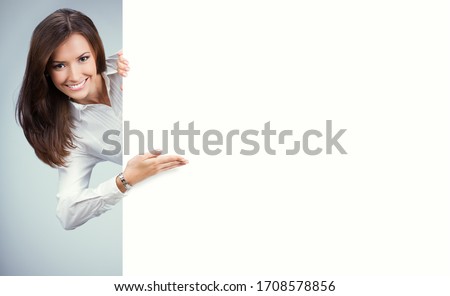 Happy young woman showing blank sign board with copy space for some slogan, text or imaginary. Business ad concept. Multiracial Asian Chinese / Caucasian model over grey background.