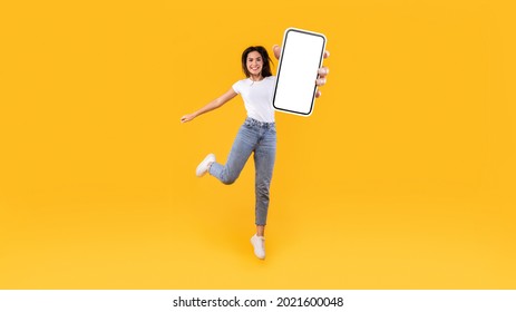 Happy young woman showing empty cellphone screen while jumping up on yellow studio background, collage, full body length, banner panorama. Excited lady recommending nice and useful mobile application - Shutterstock ID 2021600048