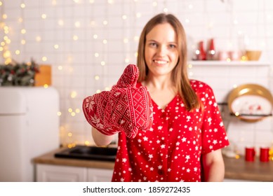 Happy Young Woman Showing Thumb Up In Xmas Oven Mitt And Smiling, Standing In Kitchen Interior Decorated For Christmas And New Year.