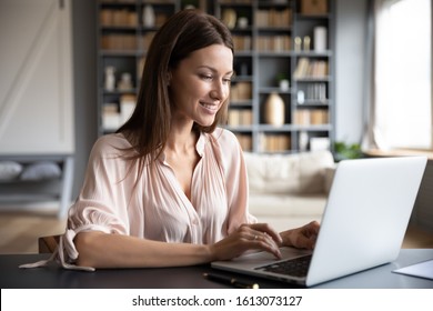 Happy young woman sit at desk look at laptop screen browsing surfing wireless Internet at home, smiling millennial female employee work on modern computer in living room, technology concept - Shutterstock ID 1613073127
