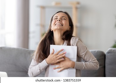 Happy Young Woman Sit On Couch Excited Receive Work Promotion Letter Or Tax Refund From Bank, Smiling Girl Student At Home Feel Euphoric Get Positive Feedback Or University Scholarship. Reward Concept