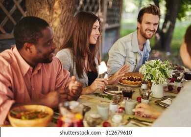 Happy Young Woman Sitting By Thanksgiving Table Among Her Friends