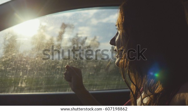 Happy young woman sitting in car passenger\
looking out window on sunny day enjoying rural car ride with lense\
flare effects. Trip.\
Vacation