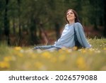 
Happy Young Woman Sitting in the Grass Enjoining Nature. Carefree person resting in a countryside field experiencing mindfulness and calmness 
