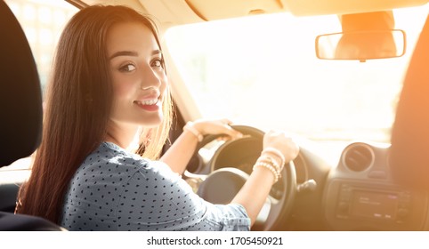 Happy young woman sitting in modern car on sunny day