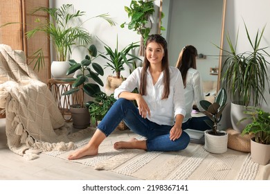 Happy Young Woman Sitting Near Mirror And Different Houseplants In Room