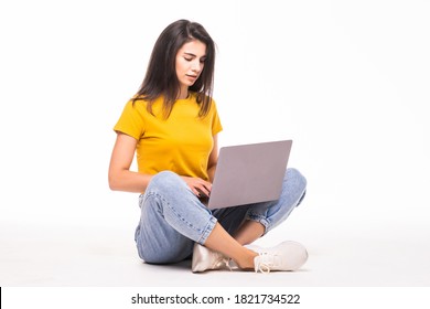 Happy young woman sitting on the floor and using laptop on white background